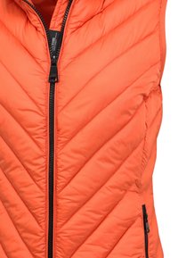 Pomarańczowa pikowana kamizelka z wzorem w jodełkę, zapinana na suwak z przodu, z bocznymi kieszeniami na suwak i czarnymi dodatkami metalowymi.