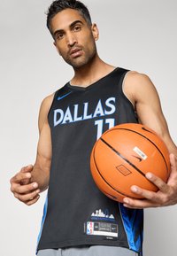 Schwarzes Basketball-Trikot mit blauer Aufschrift "DALLAS" und der Nummer "11." Enthält Nike-Logo, Etikett mit Skyline-Design und dem Schriftzug "LEGACY IS EVERYTHING."
