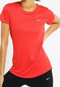 Camiseta deportiva Nike roja de manga corta, cuello redondo y ajuste ceñido. Presenta un pequeño logo gris en el pecho, en la parte superior izquierda.