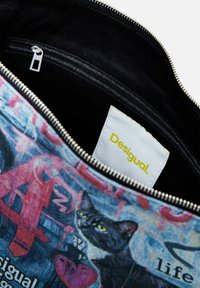 Canvas-Tasche mit einem bunten Katzenmotiv in Schwarz-, Pink- und Blautönen. Beinhaltet einen silbernen Reißverschluss und ein weißes Etikett mit "Desigual."