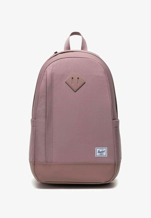 Sac à dos minimaliste mauve avec une poignée supérieure, deux poches latérales, un patch en cuir en forme de diamant et une étiquette de marque sur le bas à l'avant.