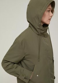Giacca cappuccio verde oliva con chiusura a zip, strings e tasche laterali. Tessuto liscio con bottoni rotondi e dettagli di cucitura a contrasto.