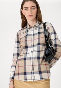 Kariertes Button-up-Hemd in Beige-, Marineblau- und Rottönen. Mit langen Ärmeln, einem spitzen Kragen und einem leichten Stoff. Trägt eine schwarze Handtasche.