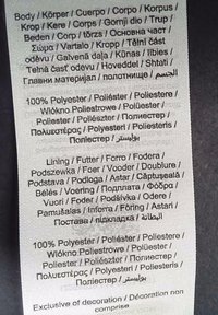 Etichette con testo nero su uno sfondo di tessuto chiaro, che elencano dettagli sui materiali e sulla foderatura in più lingue, prevalentemente poliestere.