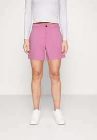 Shorts en coton rose avec une taille mi-haute, dotés de deux poches avant et d'une fermeture à bouton. Portés avec des baskets blanches et un haut à manches longues.