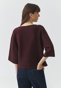 Bordeaux cropped trui met brede mouwen, voorzien van een ronde halslijn en zachte textuur. Gecombineerd met donkere denim jeans.