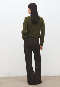 Jersey verde caqui con cintura ajustada, combinado con pantalones marrones de cuadros de talle alto. Textura suave, mangas largas, detalles sutiles de canalé.