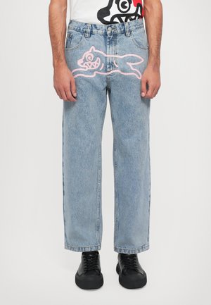 Lyseblå denimbukser med løs passform, med et rosa tegneserie-dyrdesign foran. Svarte sko brukt under.