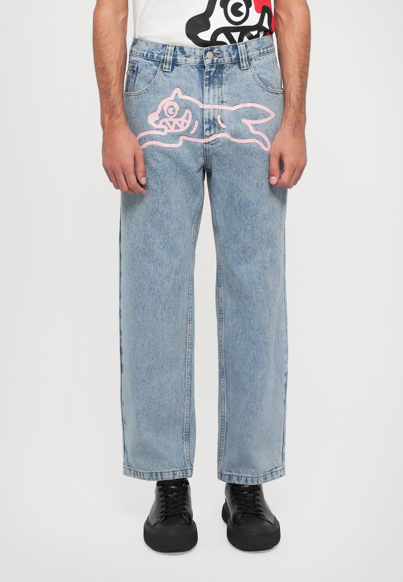 Jeans de mezclilla azul claro con un ajuste holgado, que presentan un diseño de un animal de dibujos animados rosa en la parte frontal. Zapatos negros llevados debajo.