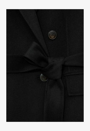 Sort uldfrakke med bindebælte, en øverste knap med en glat, mørk finish og slag med hak. Stoffet har en blød tekstur.