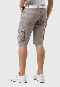 Cargo shorts in a striped pattern, beige color, featuring multiple pockets, a button closure, and a white belt. Worn with white sneakers.