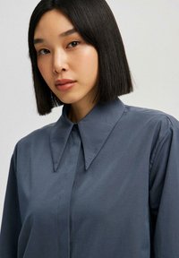 Gray collared shirt with a smooth texture, featuring a pointed collar, button-down front, and long sleeves. Simple and tailored design.