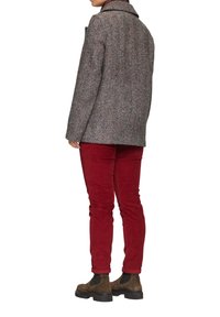 Brauner Wollmantel mit Fischgrätenmuster und breitem Kragen, kombiniert mit eng anliegenden roten Cordhosen und braunen Stiefeletten.