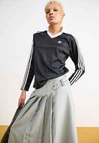 Μαύρο πουκάμισο με μακριά μανίκια και άσπρες λεπτομέρειες και λογότυπο, σε συνδυασμό με πλισέ ανοιχτό γκρίζο φούστα με διπλά μεταλλικά κούμπωμα. Υφασμάτινη υφή.