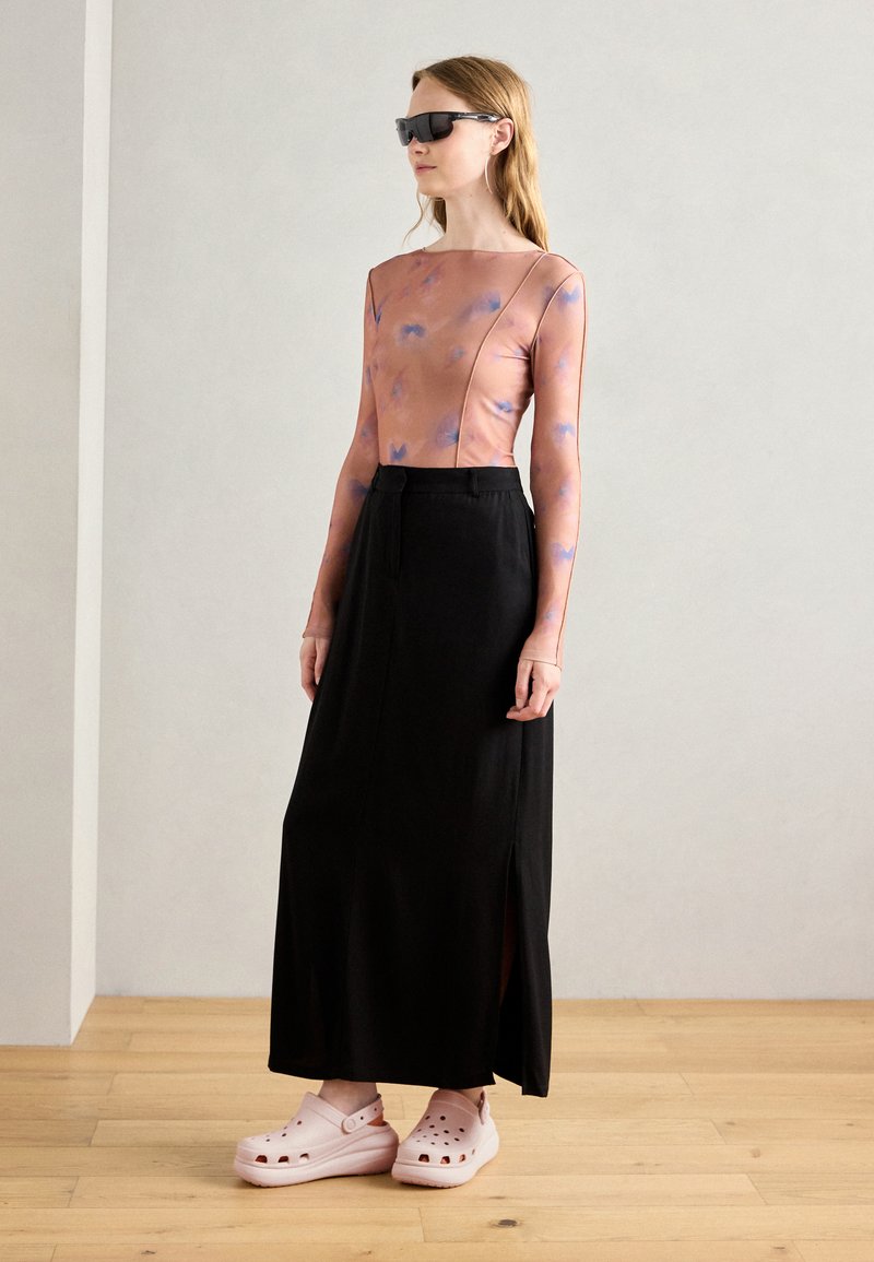 Falda negra larga con un corte lateral, combinada con una blusa de manga larga en rosa claro con patrones abstractos azules y zuecos rosas.