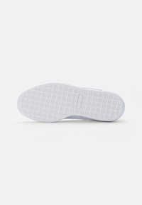 Biała podeszwa sportowego buta z fakturowanym wzorem, zawierająca małe, wypukłe gwiazdki oraz płaską, gładką krawędź. Minimalistyczny design, lekki materiał.