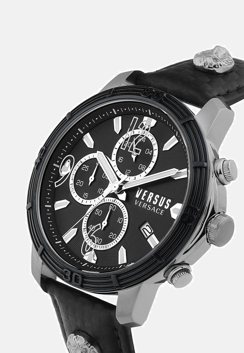 Montre chronographe Versus Versace noire et argent avec trois sous-cadrans, guichet de date, bracelet texturé et détail de crâne sur le bracelet.