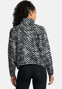 Gekürzte schwarz-weiße Jacke mit gestreiftem Muster, hohem Kragen und langen Ärmeln. Das Material wirkt glatt und leicht.