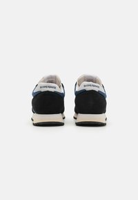 Zapatillas deportivas negras y azules con parte superior de ante y malla, con un marcado logo en el talón y una entre suela blanca, que presenta una suela exterior negra texturizada.