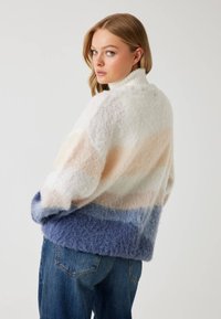 Mocha gestreepte trui van zacht, pluizig materiaal. Heeft een hoge kraag, met een verloop van crème, perzik en blauw, en een relaxed fit.