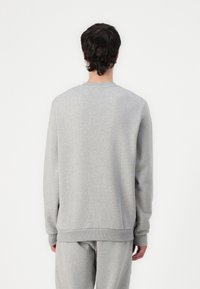 Hanorac gri cu mâneci lungi, decolteu și manșete ribbate. Textură moale, design simplu și croială lejeră, asortat cu pantaloni corespunzători.