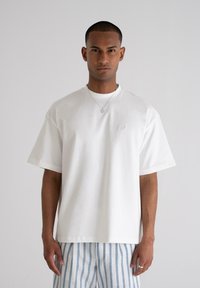 White cotton t-shirt with a relaxed fit, short sleeves, and a subtle logo on the chest, paired with blue and white striped trousers.