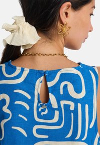 Μπλε και κρεμ φόρεμα με σχέδιο, με άνοιγμα στην πλάτη σε σχήμα κλειδαρότρυπας. Διαθέτει χρυσή αλυσίδα λαιμού και λευκό υφασμάτινο λαστιχάκι για τα μαλλιά με υφή.