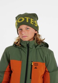 Grüne und orange isolierte Jacke mit Kapuze, mit einem Reißverschluss und Logo. Die Strickmütze ist grün mit gelber Schrift.
