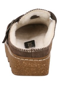 Chaussure en suede marron à enfiler, avec une douce doublure en fourrure crème et une semelle en liège texturée. Présente des détails de couture robustes et un accent en métal.