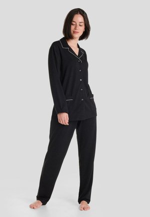 Conjunto de pijama negro que incluye una camisa de botones con ribetes blancos en contraste y bolsillos laterales, acompañada de pantalones holgados. Tela suave, ajuste relajado.