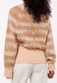 Suéter de punto con un patrón de rayas beige y marrón claro, tela texturizada y dobladillo acanalado. Mangas largas y ajuste relajado.