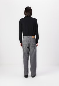 Black long-sleeve shirt paired with loose-fitting gray jeans. Jeans feature back pockets and a brown leather patch on the waistband.
