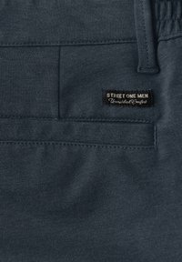 Ciemnoszare męskie spodnie z elastycznym pasem, widocznymi przeszyciami, tylną kieszenią oraz czarną metką z napisem "STREET ONE MEN Unmatched Comfort."