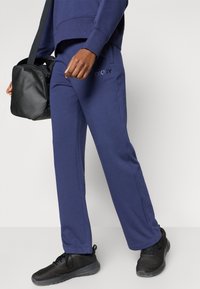 Granatowe dresy o luźnym kroju, z logo DKNY i bocznymi kieszeniami, połączone z czarnymi siateczkowymi sneakersami i czarną torbą na ramię.