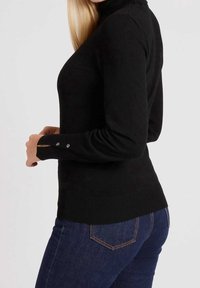 Pull en col roulé noir avec des manches longues, comportant des boutons décoratifs sur le poignet, fabriqué dans un matériau doux et léger.