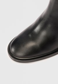 Sort læder ankelstøvle med en glat overflade, rund tå og detaljeret syning langs sålen. Enkel, strømlinet design.