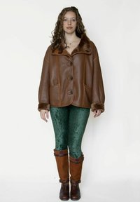 Bruine leren jas met nepbontkraag en -manchetten, voorzien van decoratieve stiksels, gecombineerd met groene fluwelen legging en bruine laarzen tot aan de knie.