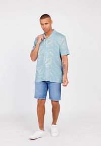 Kurzarmhemd in Hellblau mit grünem Blattmuster, kombiniert mit Jeansshorts und weißen Sneakers, mit einem Button-Down-Kragen.