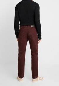 Pantaloni di cotone bordeaux con vestibilità slim, design a cinque tasche e finitura leggermente strutturata. Presentano una toppa con logo sulla cintura posteriore.