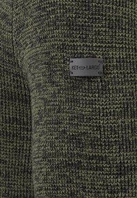 Gebreide trui in donkergroen met zwarte spikkels. Bevat een textuurpatroon en een klein zwart logo label dat is genaaid.