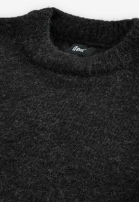 Dunkelgrauer Strickpullover mit ribbeltem Kragen, strukturierter Oberfläche und sichtbarem Flusen, aus einem wollähnlichen Material gefertigt. Markenschild im Kragen.