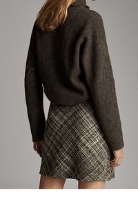 Maglione di lana marrone con collo alto, abbinato a una mini gonna a quadri con texture in toni neutri di marrone e grigio.