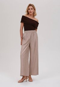 Braunes Off-Shoulder-Oberteil kombiniert mit beigen, gestreiften Hosen mit weitem Bein. Die Hose hat einen elastischen Bund; beide Teile sind leicht.