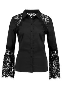 Blouse noire boutonnée avec panneaux en dentelle sur les épaules et manches évasées en dentelle, comportant des motifs floraux et un col classique.