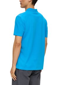 Türkises Polohemd mit kurzen Ärmeln und Kragen, aus Baumwollstoff, glatte Textur, von hinten betrachtet, kombiniert mit dunklen Shorts.