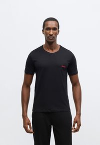 Čierne tričko s krátkym rukávom z bavlny, s okrúhlym výstrihom a malým červeným logom "HUGO" na hrudi. Hladká textúra a priliehavý strih.