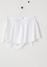 Shorts de sport légers blancs avec taille élastique suspendus sur un mur blanc avec trois punaises visibles.