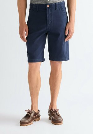 Marineblå bomuldsshorts med knaplukning, lige snit og opsmøgede kanter, kombineret med brune lædersko med snørebånd og teksturerede såler.