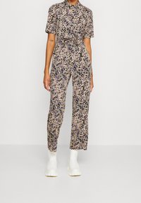 Combinaison florale à manches courtes, fond noir, petites fleurs multicolores, taille ceinturée et jambes ajustées. Associée à des bottes blanches à semelles épaisses.