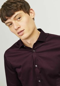 Donker kastanjebruin knoopshirt met een strak kraag, met een gladde textuur en subtiele glans, aangevuld met lichtgekleurde knopen.